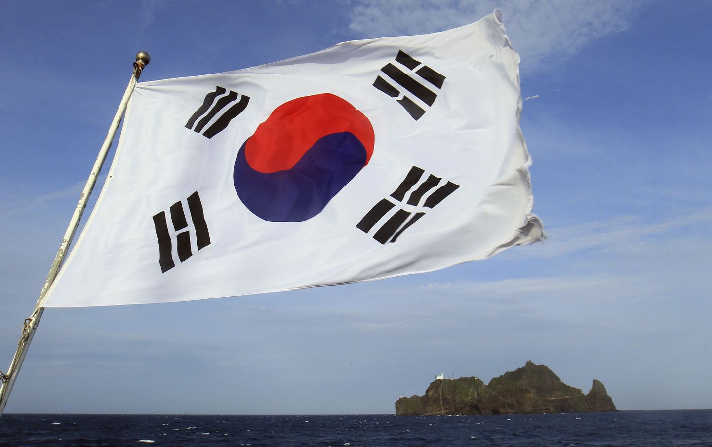 Esiplaanil Lõuna-Korea riigilipp, taga paistab üks Takeshima ehk Dokdo saartest.