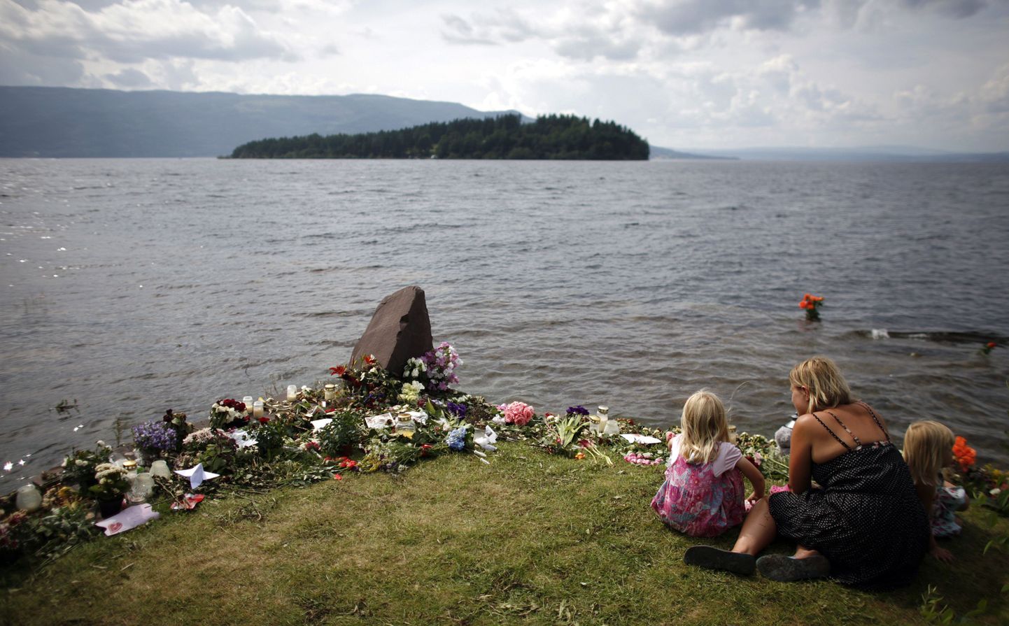 Naine on koos tütardega Tyrifjordeni järve kaldal lillede juures, mis on toodud Utøya saare (paistab eemalt) veresauna ohvrite mälestuseks.