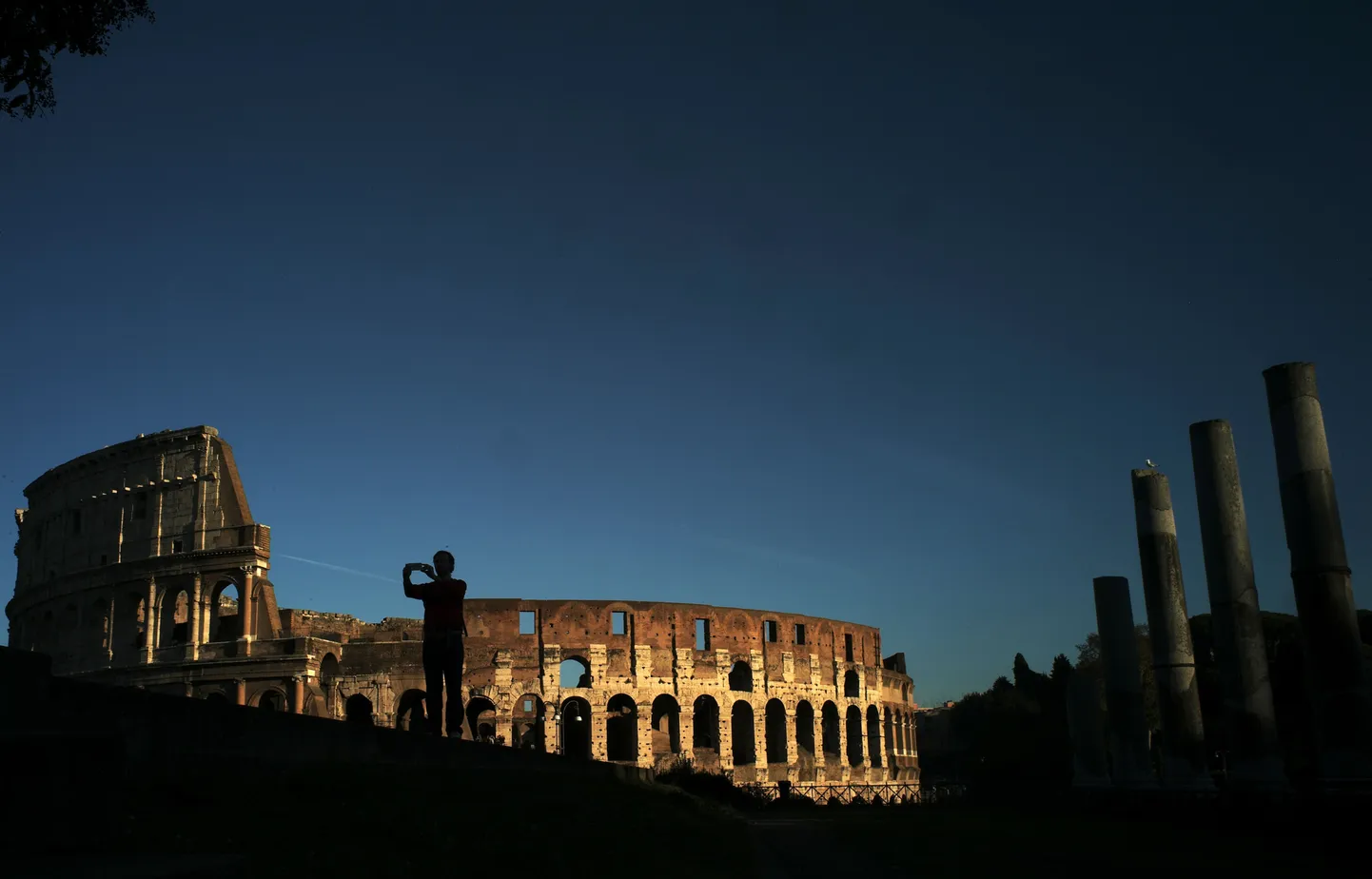 A man takes pictures near the Colosseum at sunset on November 21, 2014 in Rome.  AFP PHOTO / FILIPPO MONTEFORTE