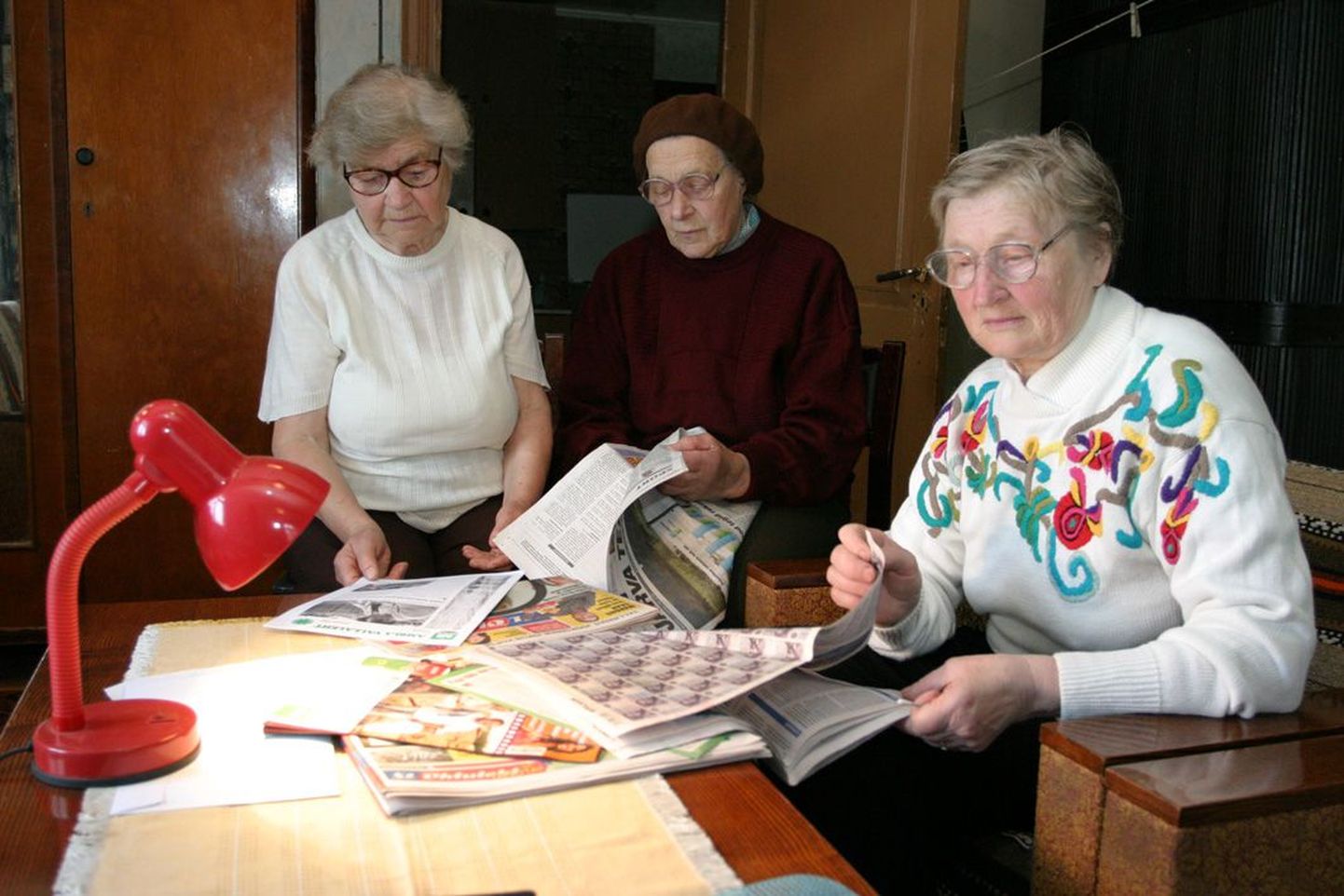 Kukevere küla eakad Leili Kaseväli (vasakult), Aino Tulvik ja Maie Boisen jälgivad murelikult ajalehti, lootes leida uudist, mis tulevikku heledamates toonides näitaks. Pilt on illustratiivne.
