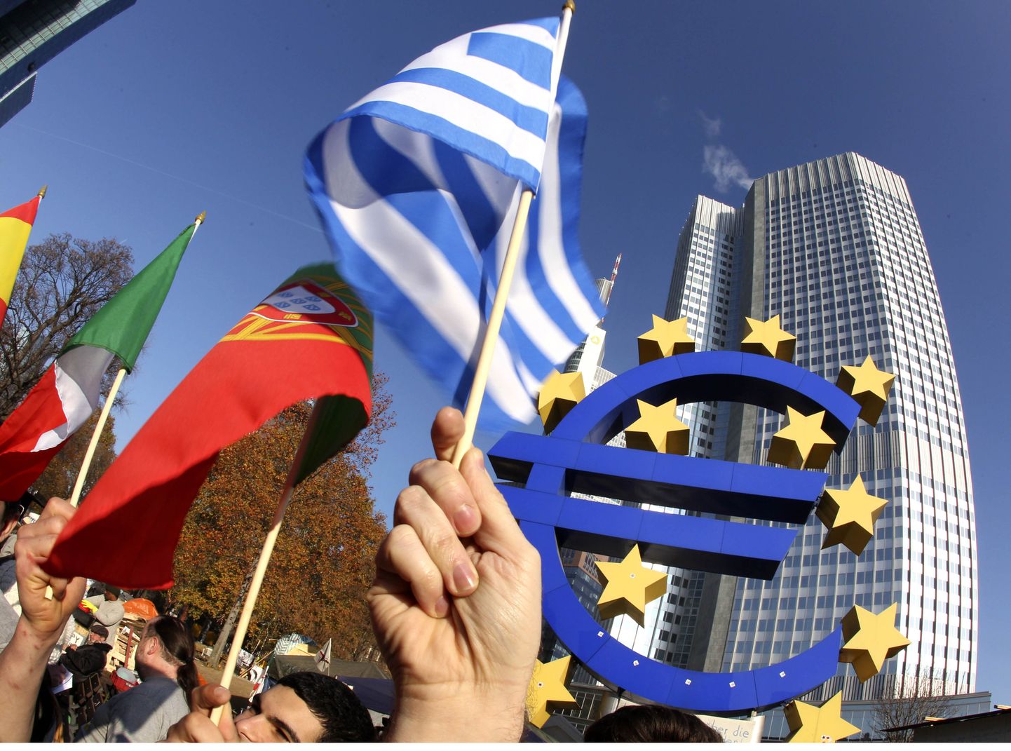 Флаги Греции и Португалии на фоне символа евро и здания ЕЦБ.