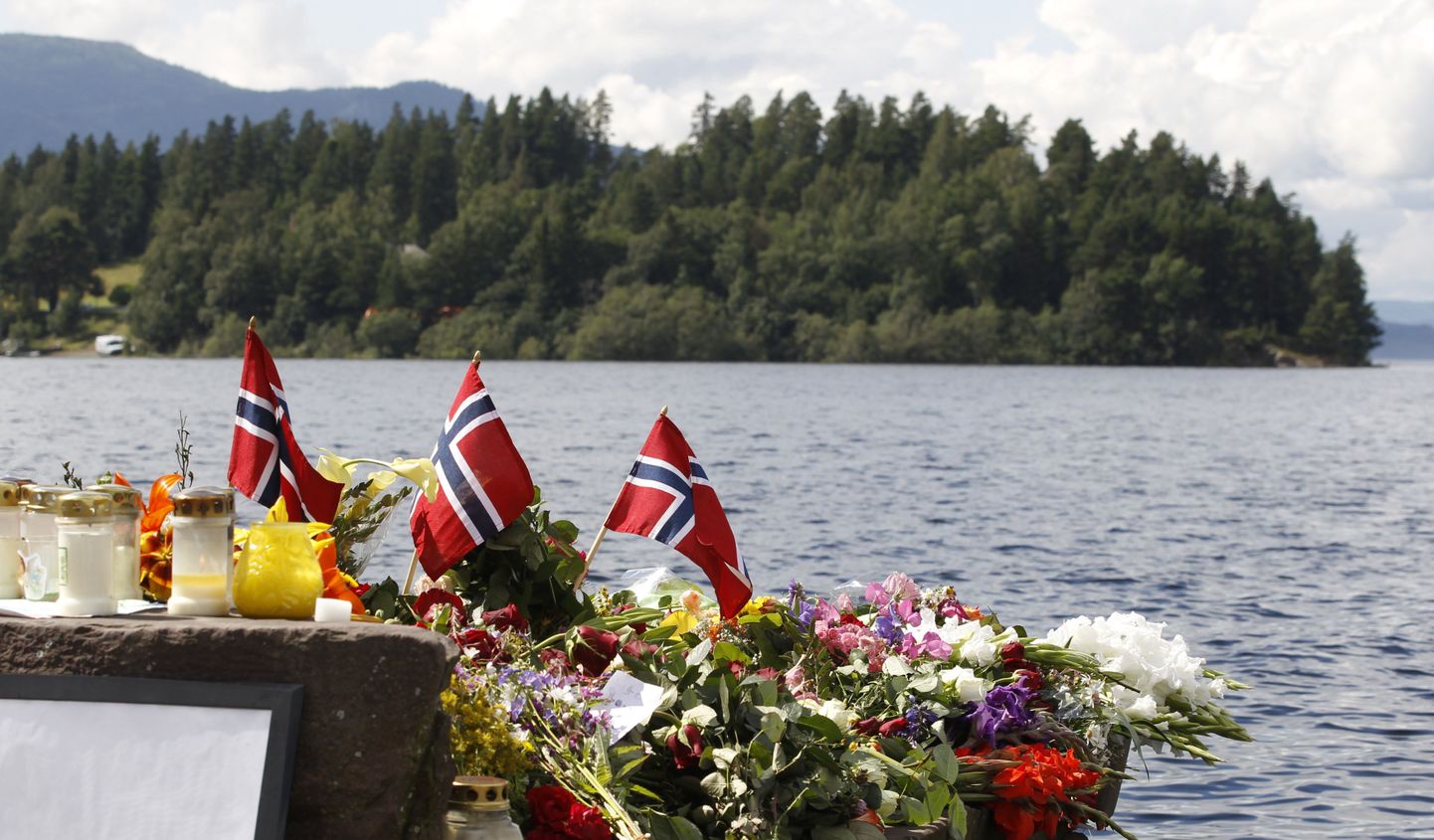 Veretöös hukkunute mälestuseks toodud lilled, küünlad ja rahvuslipud Utøya väikesaare taustal.