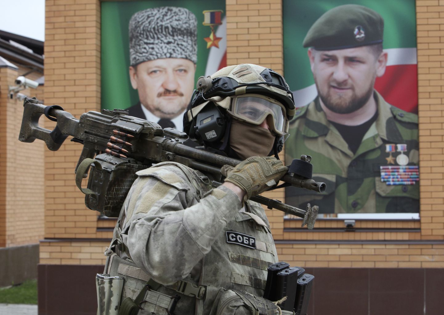 Член группы быстрого реагирования «СОБР», подчиняющейся российскому Министерству внутренних дел. На заднем плане портрет президента Чечни Рамзана Кадырова (справа) и его отца Ахмада Кадырова (справа), предыдущего руководителя Чечни, погибшего в 2004 году в результате теракта.