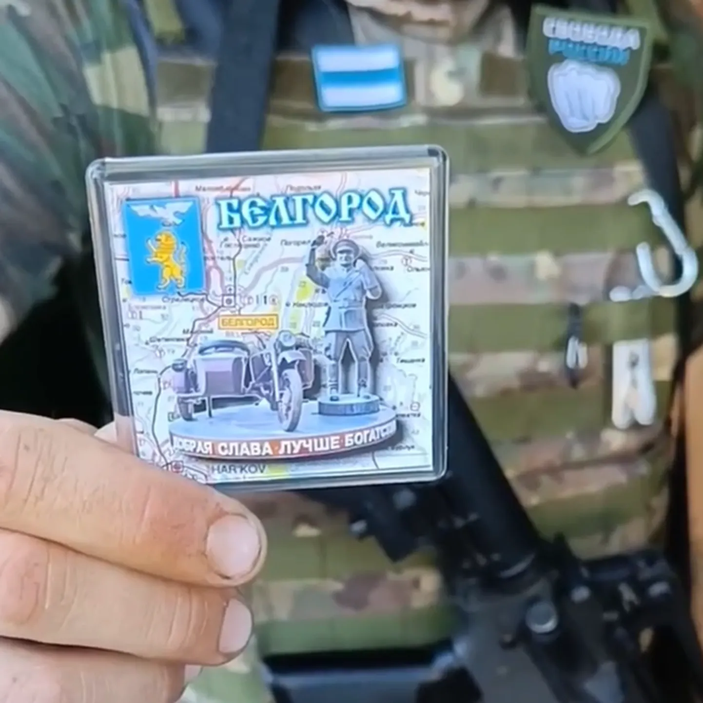 Боец с символикой легиона "Свобода России" держит в руке трофейный сувенирный магнит с гербом Белгорода во время военной операции на территории Белгородской области, июнь 2023 года.