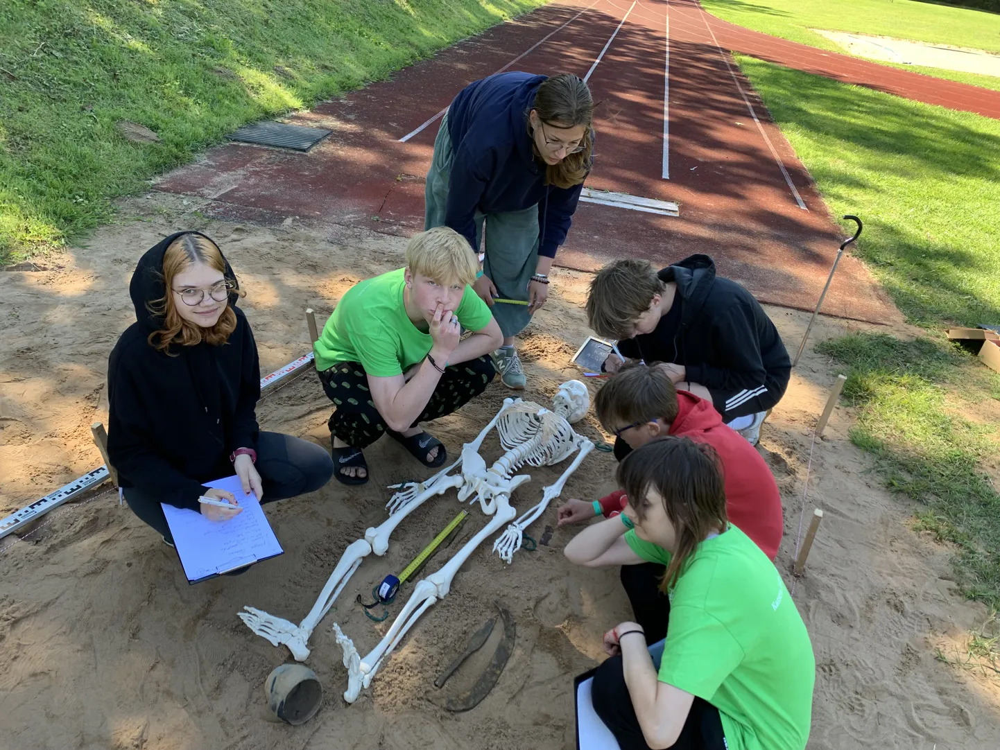 Laagris osalejad uurivad kooli staadioni kaugushüppekastis lebavat skeletti.