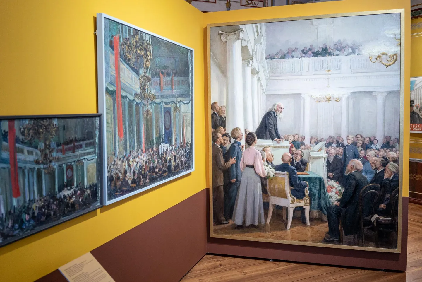 Leili Muuga maali «Keemik Dmitri Ivanovitš Mendelejev tervitab Tartu ülikooli 100. aastapäeval» (1953, paremal) kõrval ripub vaheseinal Elmar Kitse «1. mai aktus Tartu riikliku ülikooli aulas» (1945) ja omakorda selle kõrval on sama maali kavand.