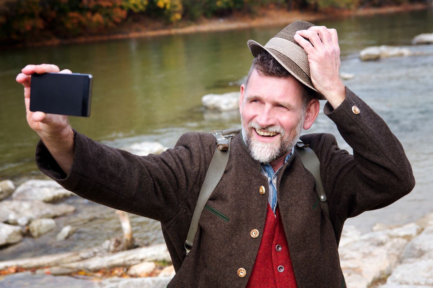 bavarian man in his 50s standing by river and taking a selfie