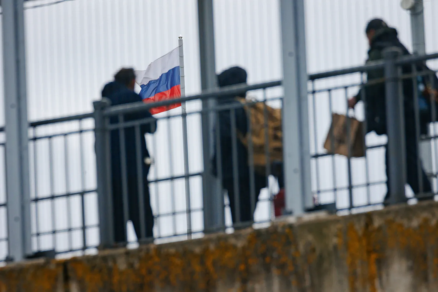 Путешествующие через эстонско-российскую границу люди на нарвском пограничном мосту. Флаг России встречает их на восточном берегу реки Нарва.
