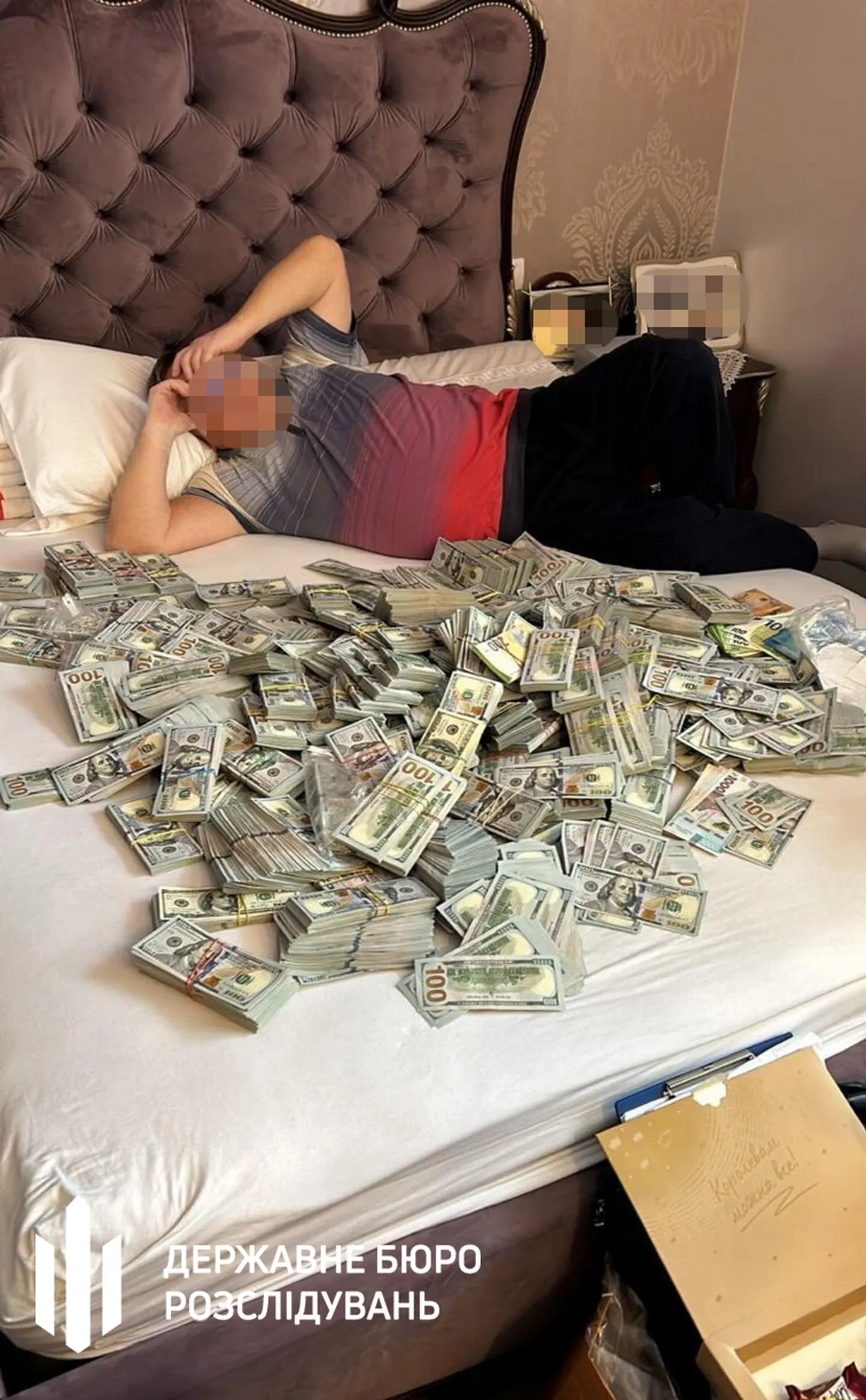 ​Ukraina Riikliku Uurimisbüroo veebilehel avaldatud foto mehest rahapakkide keskel.