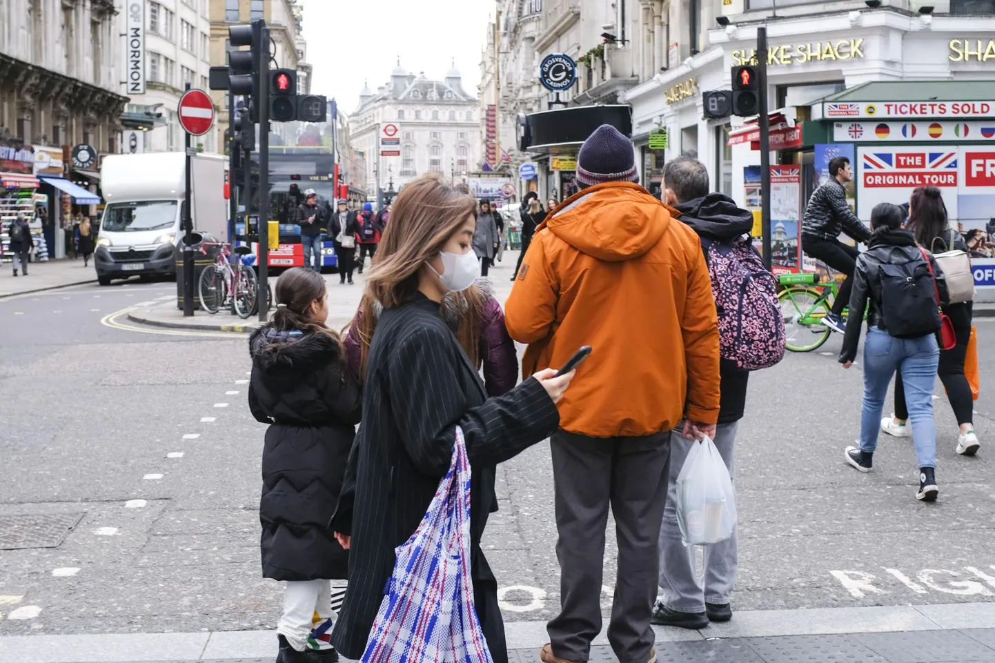 Londoni tänaval kõndiv naine püüab end koroonaviiruse eest kaitsta näomaski kandes, ent mobiiltelefonis ohustavad teda kulutulena levivad libauudised.