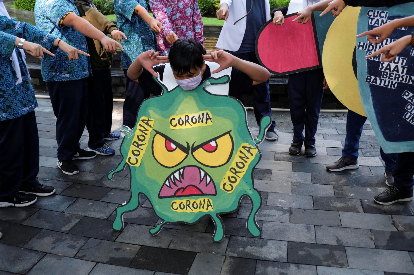 Õpilased Indoneesias koroonaviirust kujutava plakatiga.