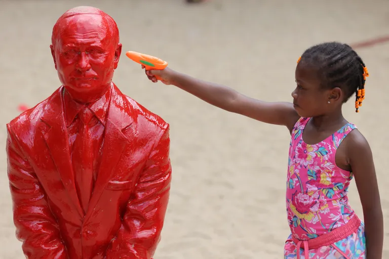 Ребенок приставляет дуло игрушечного постолета к веску красной скульптуры Путина. REUTERS/Andrew Kelly
