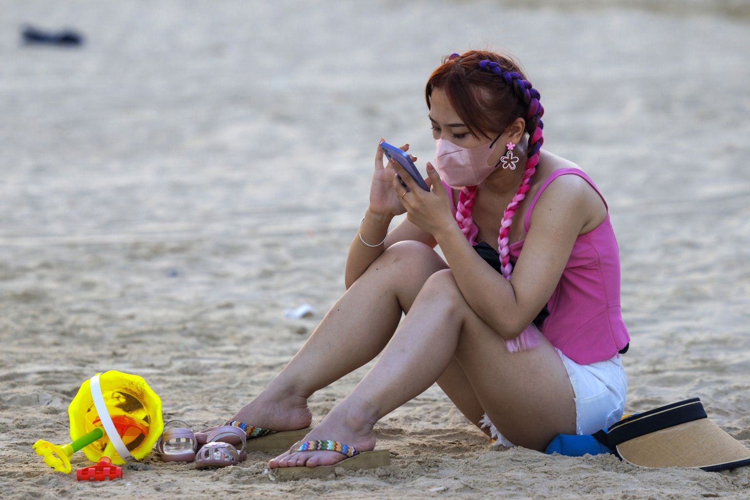 Kaitsemaski kandev naine istub Hainanis Houhai rannas.