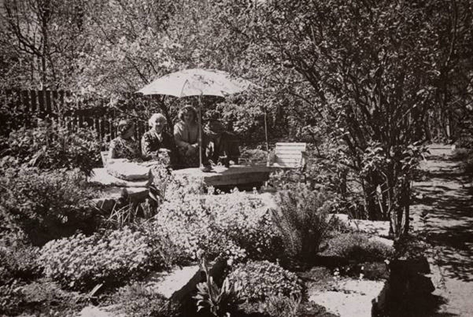 Elo ja Friedebert Tuglas ning Elo Kurvits päikesevarju all aias (1959).