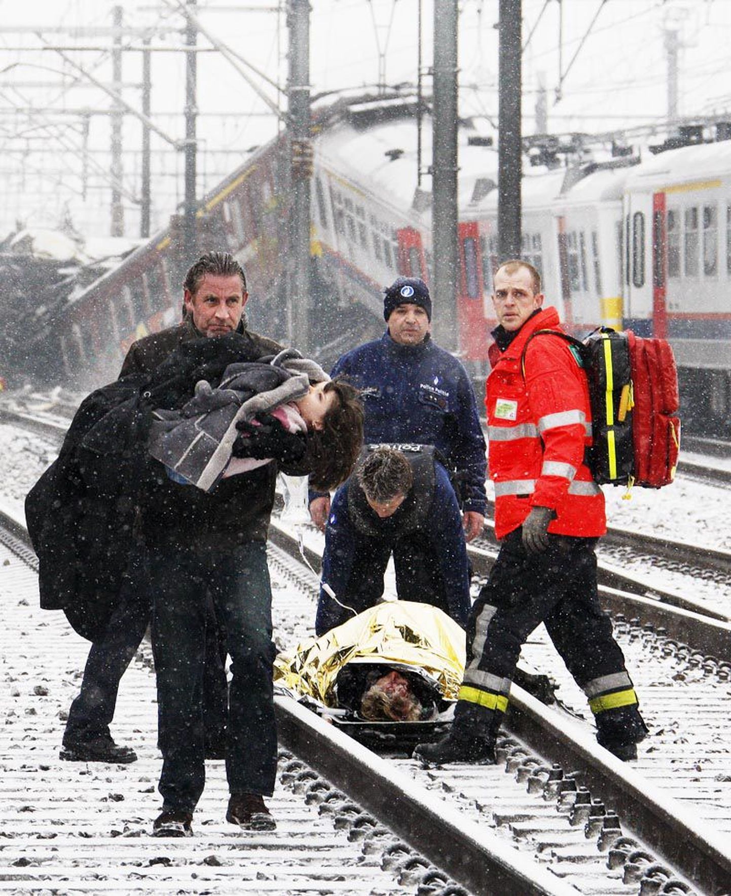 Mees kõnnib, laps süles, õnnetuskohast eemale. Taustal abistavad päästjad üht enam kui sajast eilses Brüsseli rongiõnnetuses kannatada saanud inimesest.
