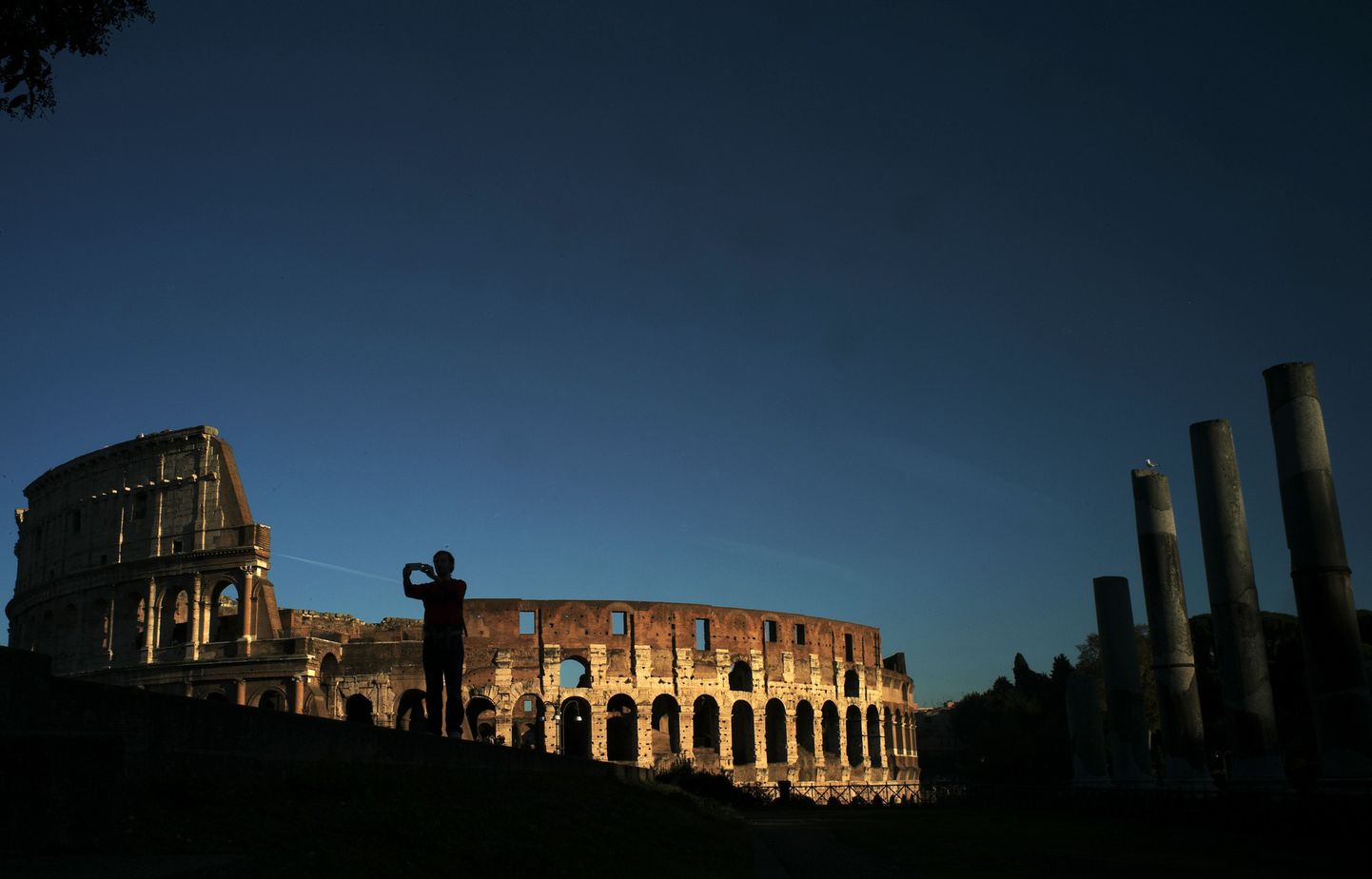 A man takes pictures near the Colosseum at sunset on November 21, 2014 in Rome.  AFP PHOTO / FILIPPO MONTEFORTE