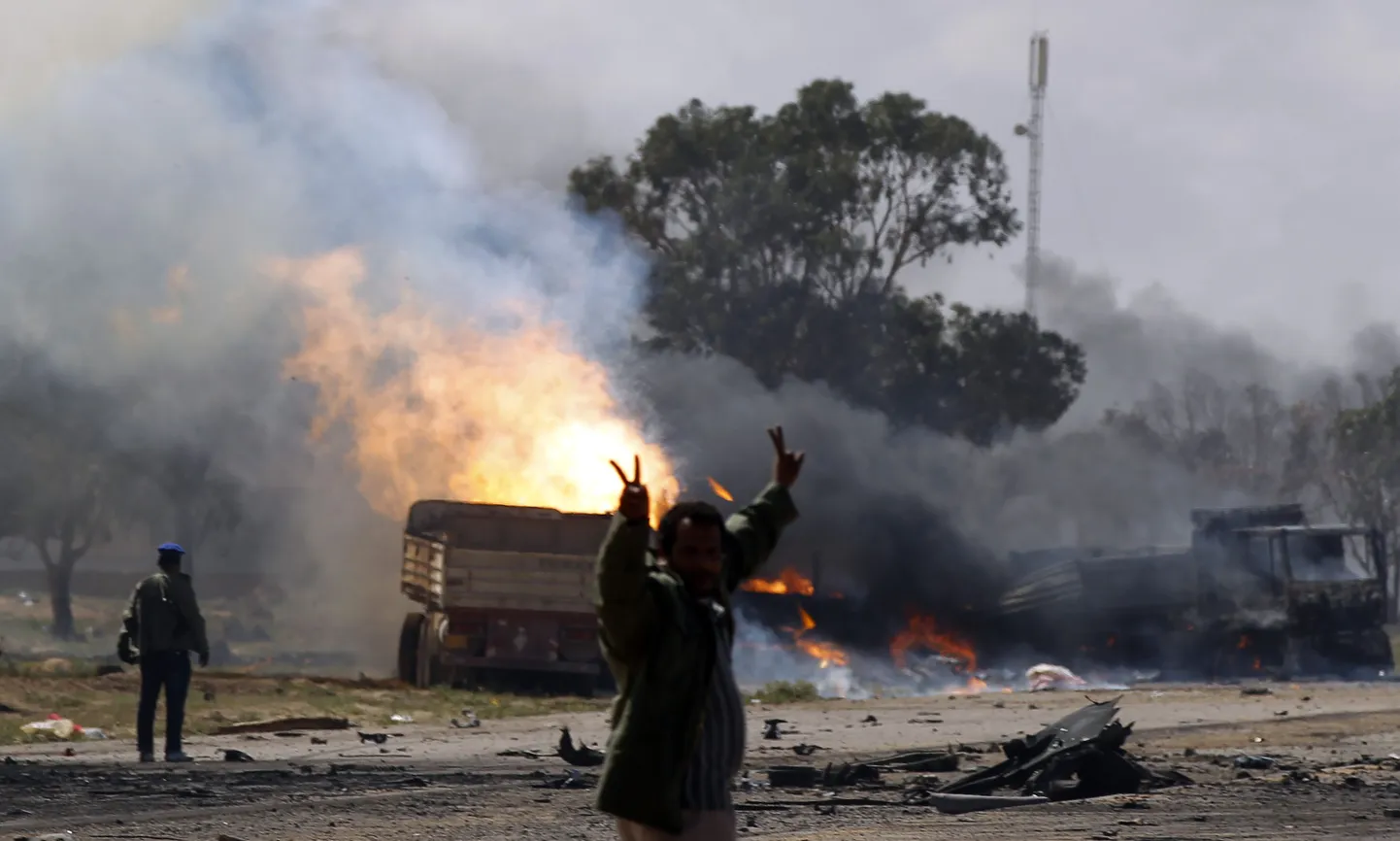 Gaddafi toetaja põlevate sõidukite taustal pärast liitlasvägede õhurünnkut.