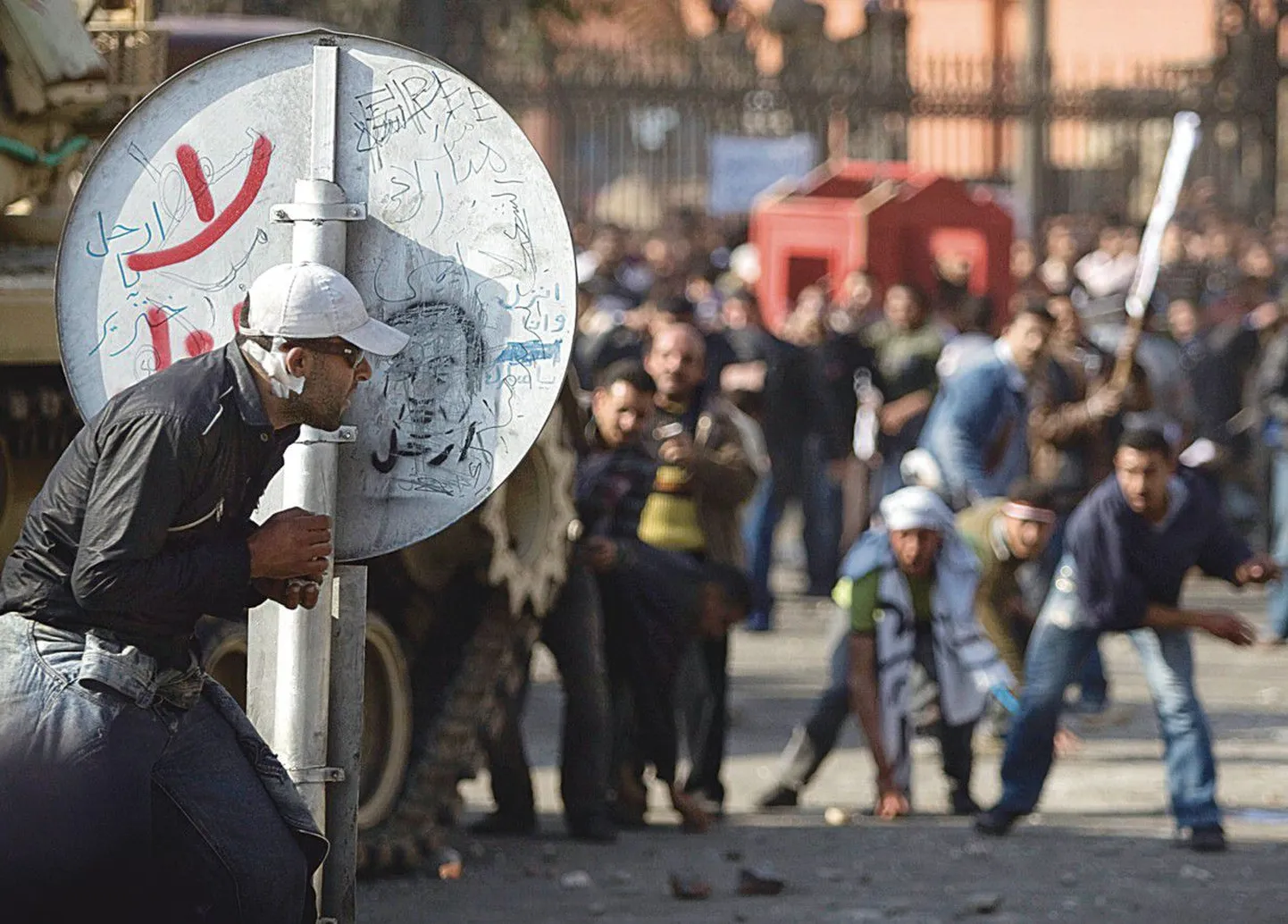 Противник режима президента Мубарака пытается укрыться от града камней за дорожным знаком.