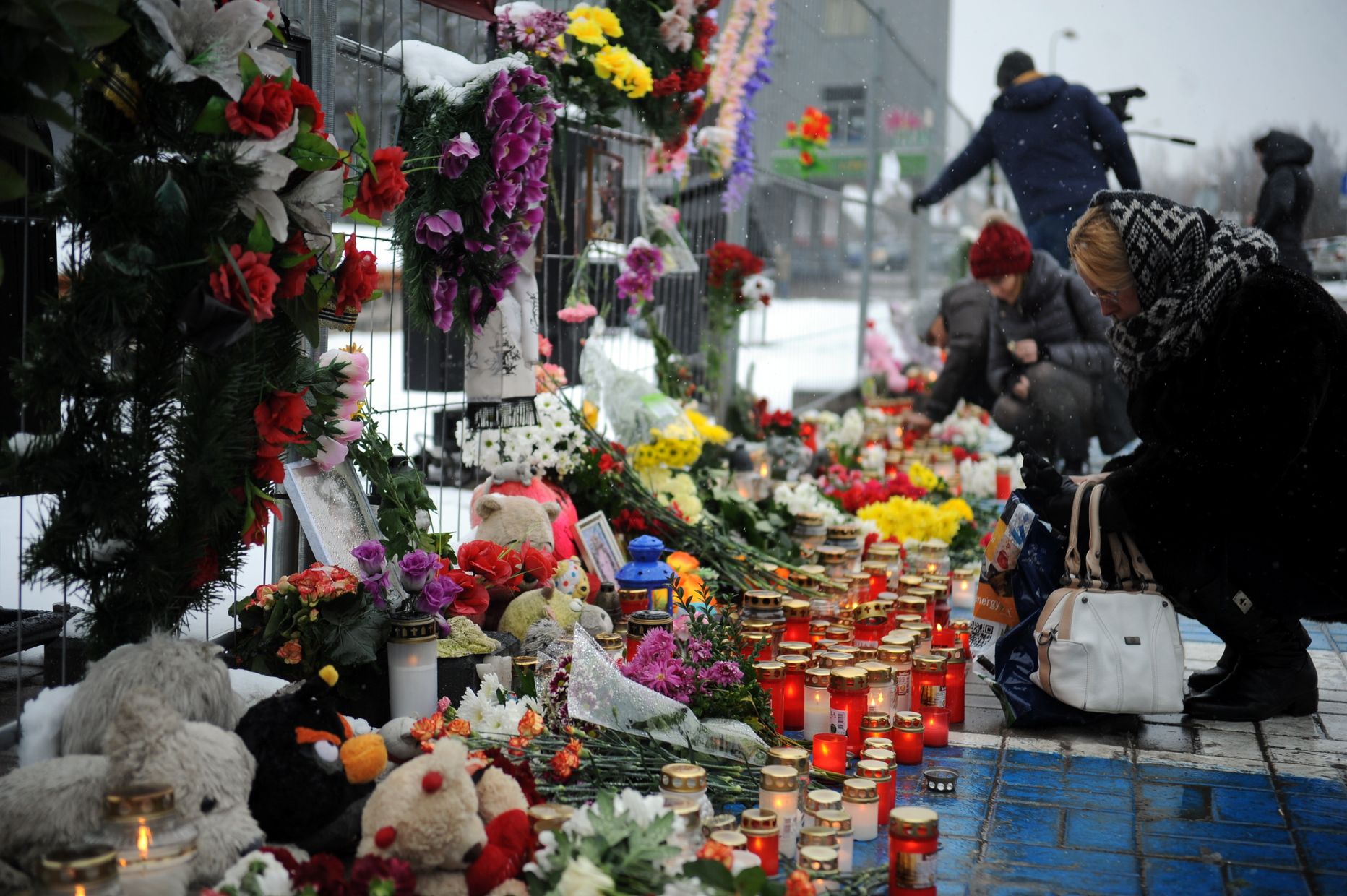 Cilvēki noliek ziedus un iededz svecītes Zolitūdes traģēdijas vietā.