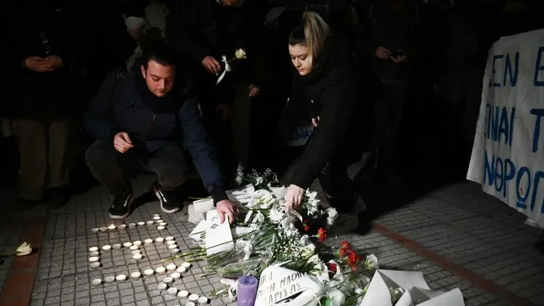 Люди зажигают свечи и возлагают цветы у железнодорожного вокзала в Ларисе в среду