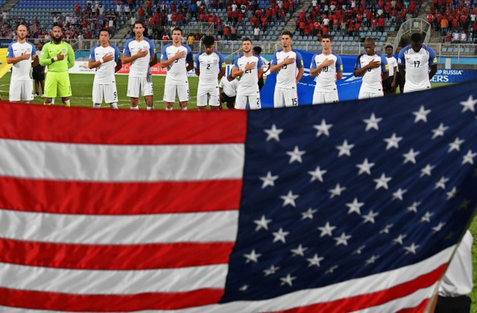 ASV izlases futbolisti himnas atskaņošanas laikā, stāvot aiz savas valsts karoga