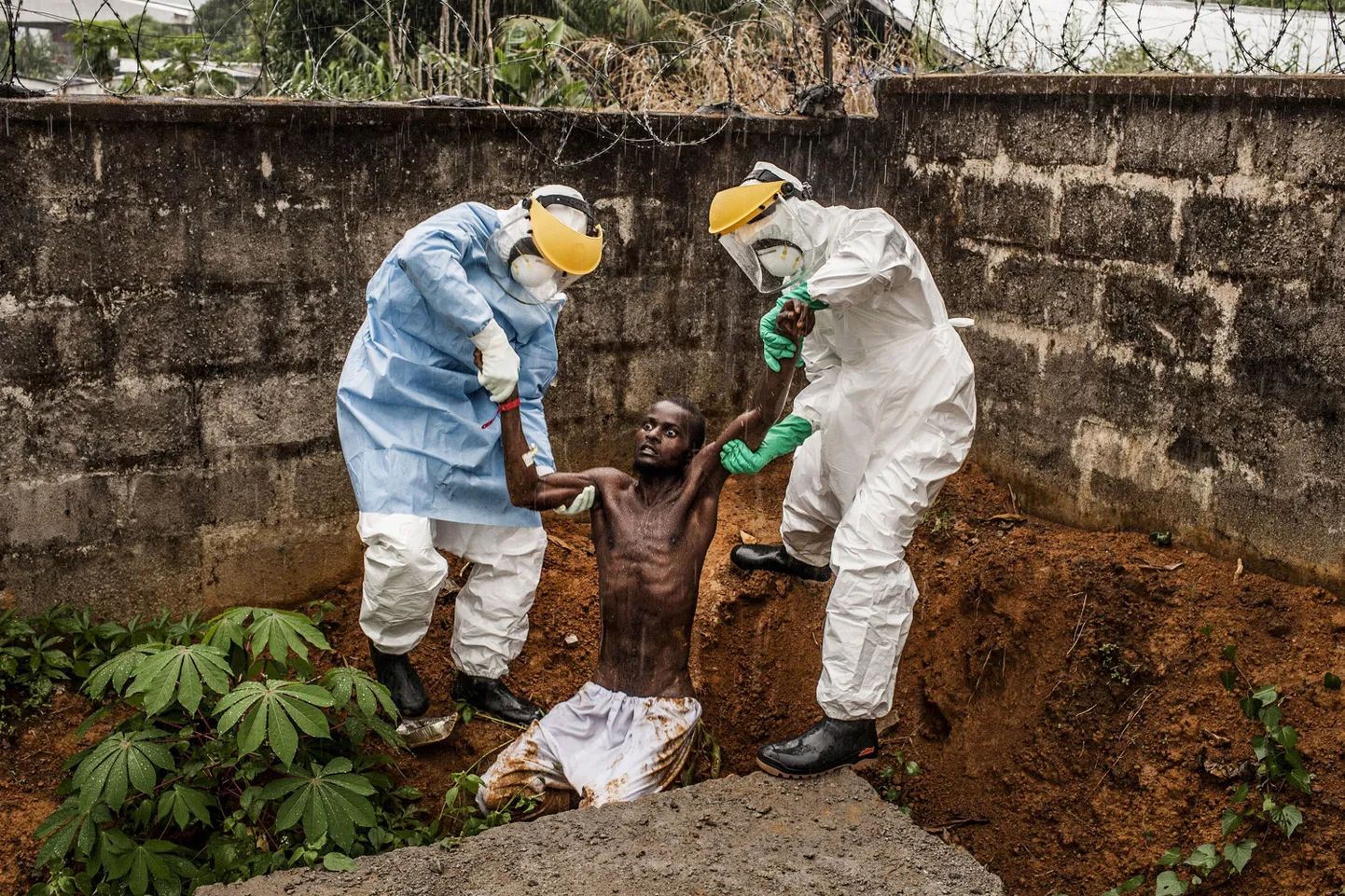 Fotograaf Peter Muelleri maailma pressifoto konkursil auhinnatud fotol püüavad kaitsevarustuses meditsiinitöötajad aidata Ebola tekitatud deliiriumisse langenud meest.