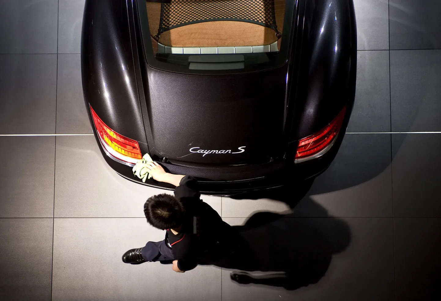 Mees puhastab müügisaalis olevat Porsche Cayman S sõiduautot.