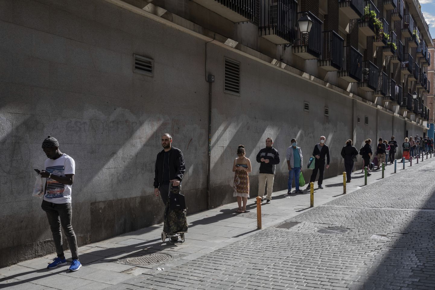 Cilvēki Madridē stāv rindā uz veikalu, ievērojot divu metru distanci.