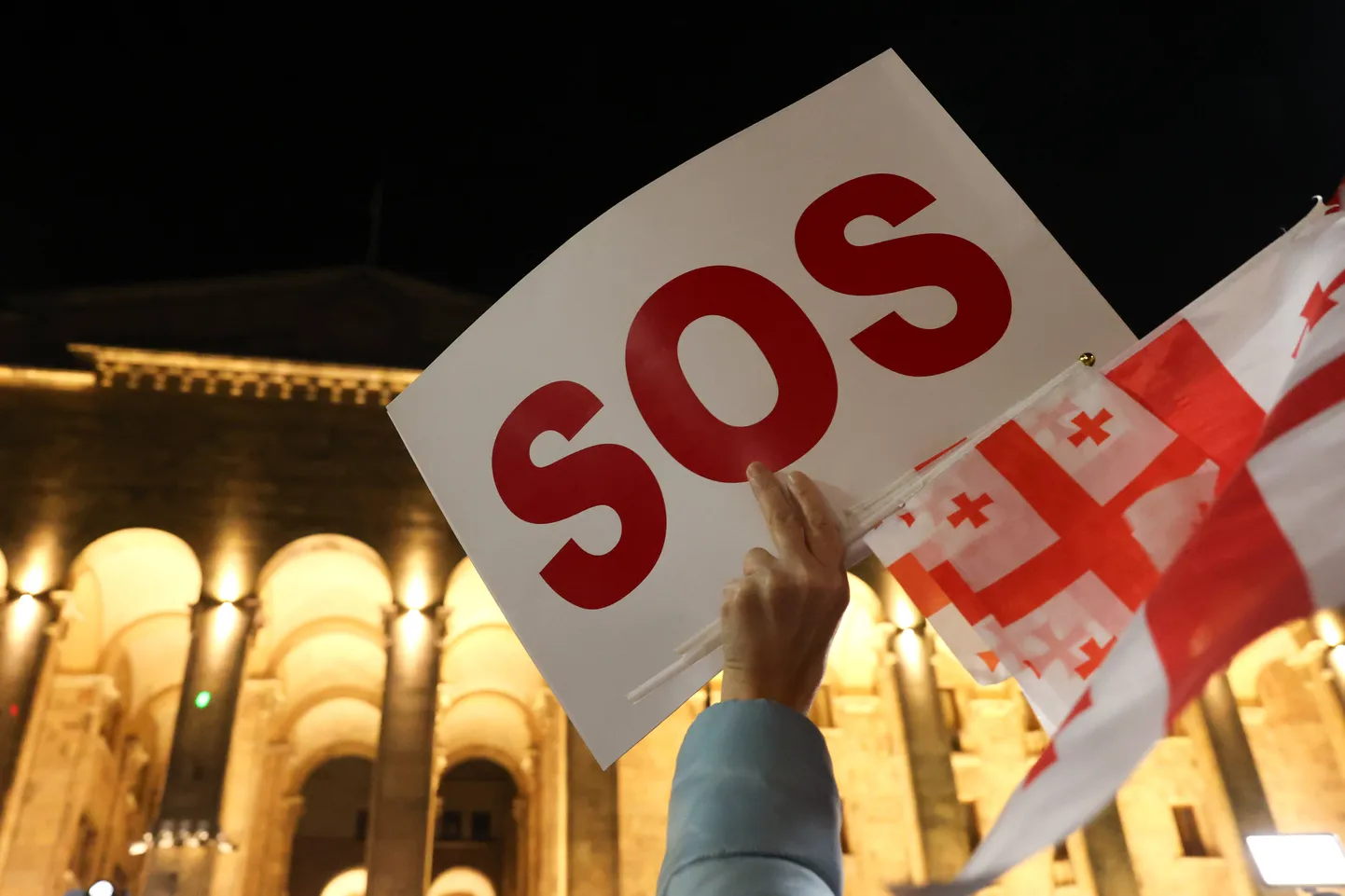 Участник акции оппозиции в Тбилиси держит плакат с надписью SOS (спасите наши души), 28 октября 2024 года.