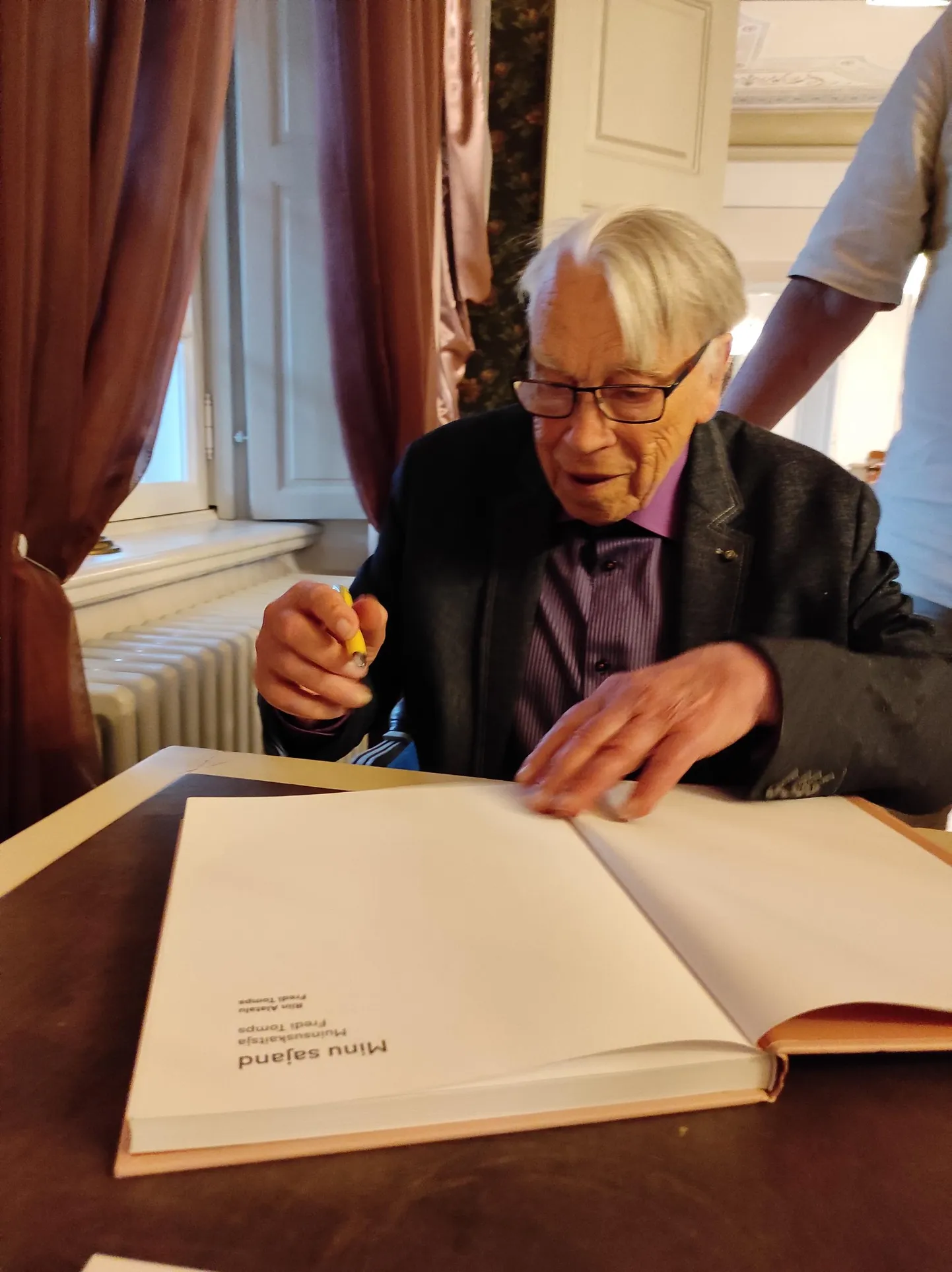 Fredi Tomps raamatusse "Minu sajand" lahkesti autogramme jagamas.