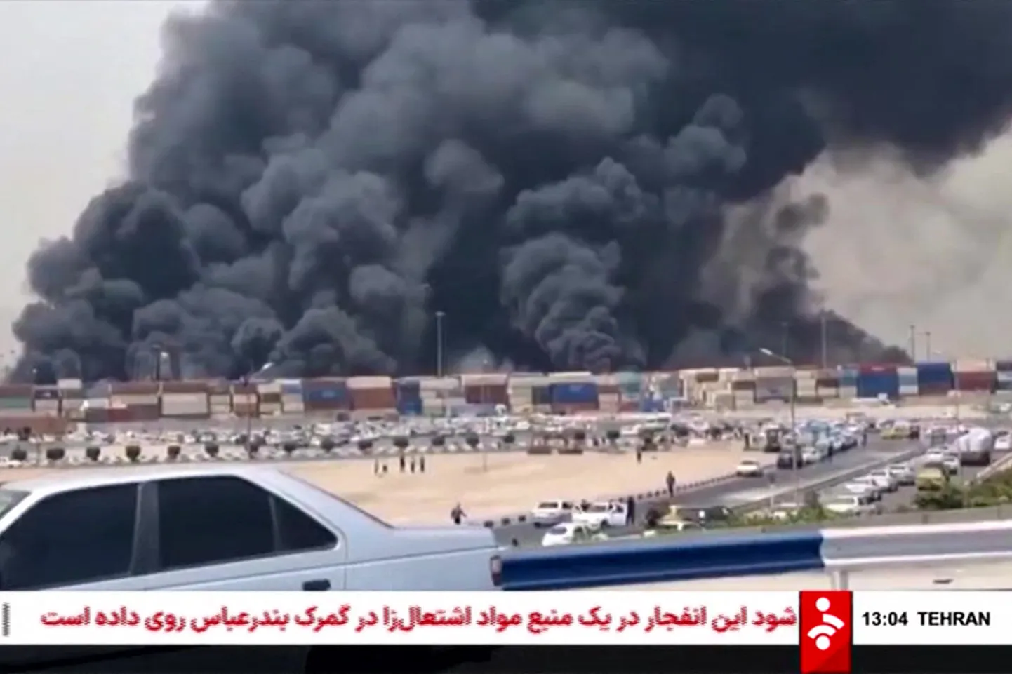 Šis attēls ir iegūts no kadriem, ko 2025. gada 26. aprīlī publicējusi Irānas valsts televīzija Islamic Republic of Iran Broadcasting News (IRIBNEWS), un tajā redzami biezi melni dūmi, kas ceļas pēc sprādziena Šahida Radžai ostas piestātnē, uz dienvidrietumiem no Bandarabasas Irānas Hormozgānas provincē.