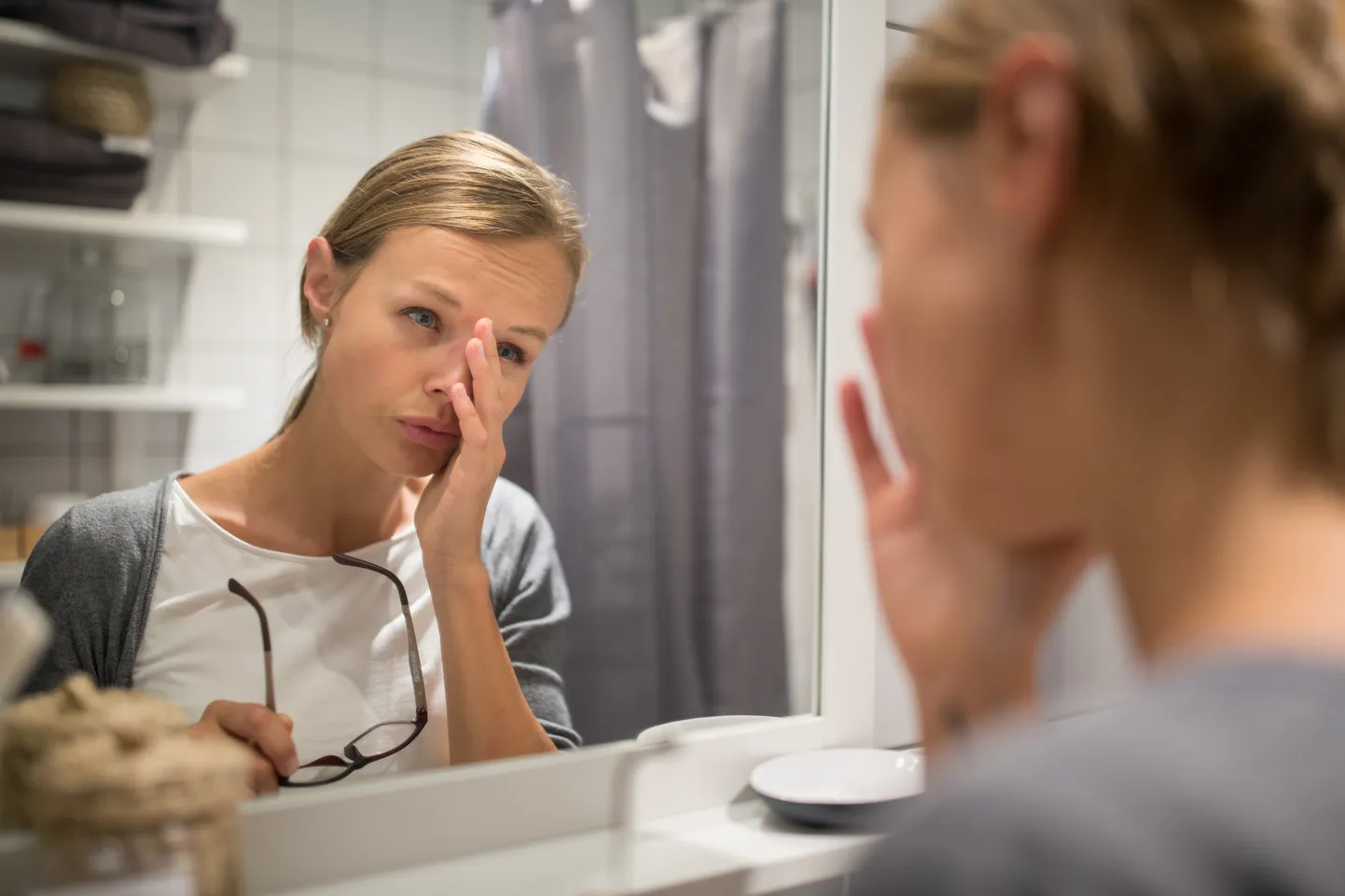 Groggy, young woman yawning in front of her bathroom mirror in the morning - trying to wake up and get ready for work (color toned image; shallow DOF)