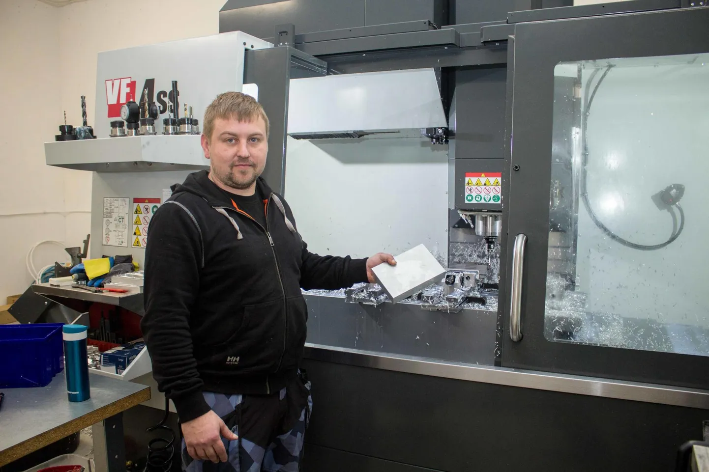 P-Tech OÜ juht Peep Vare näitab alumiiniumitükki, mis tema selja taha jäävas freesiaparaadis vajaliku kuju saab.