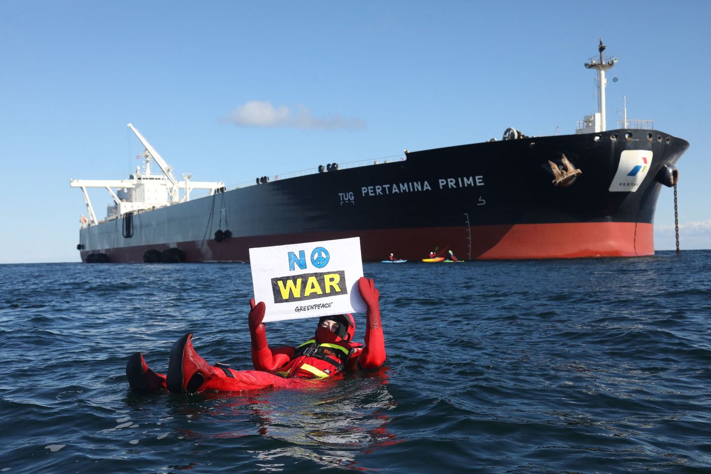 Merepäästekostüümis Greenpeace aktivist sõjavastase plakatiga takistab Venemaa naftat vedava laeva pardumist Singapuri tankeri Pertamina Prime külge. Taamal Greenpeace liikmed kajakkidel.