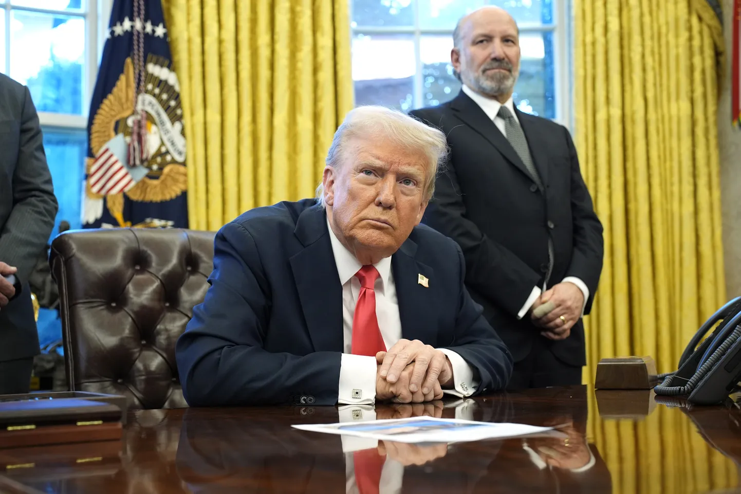 USA president Donald Trump rääkimas 25. veebruaril 2025 Washingtonis Valges Majas ovaalkabinetis meedia esindajatega. Tema taga seisab USA kaubandusminister Howard Lutnick.