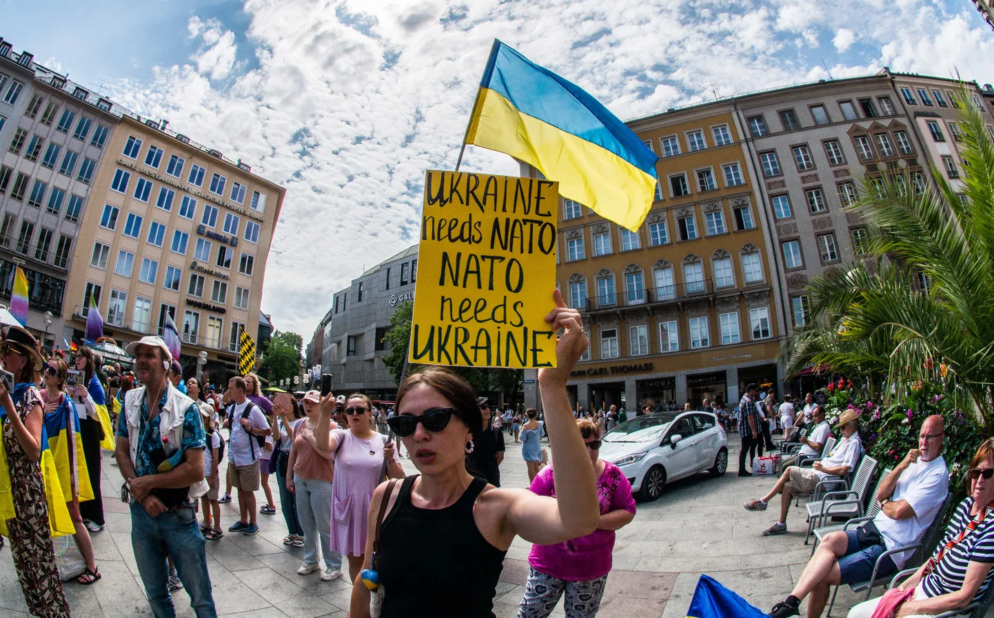 NATO tippkohtumise eel Vilniuses toimuvad Euroopas meeleavaldused Ukraina vastuvõtmise nimel liitu. Pildid meeleavaldaja 8. juulil 2023. aastal Saksamaaal Münchenis plakatiga «Ukraina vajab NATOt, NATO vajab Ukrainat»