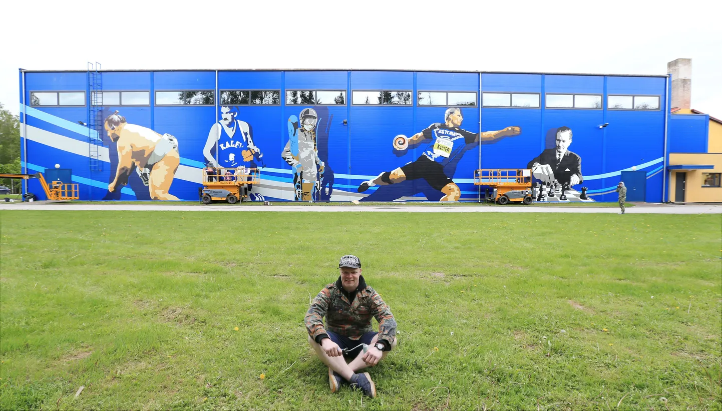 Kristjan Bachman alias Bach Babach võttis valmiva hiigelmaalingu ees korraks istet. Tema selja taga on spordihoone juures tõstukitel töötavad tudengid ja seinal spordikuulsused Baruto, Tiit Sokk, Kelly Sildaru, Gerd Kanter ja Paul Keres. Erki Nool ja Erika Salumäe portree on otsaseinal.