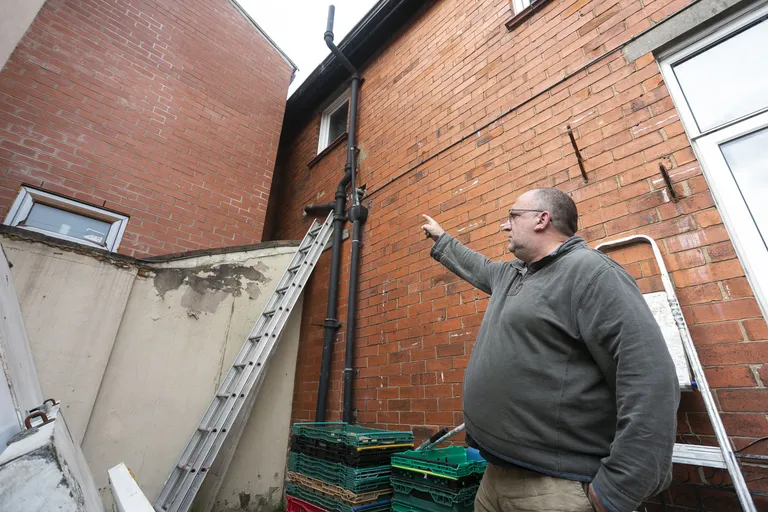 Neal näitab hoovi poolt, kuidas naabrite juurdeehitus tema maja (paremal) aknaid loomuliku valguse eest varjutab.