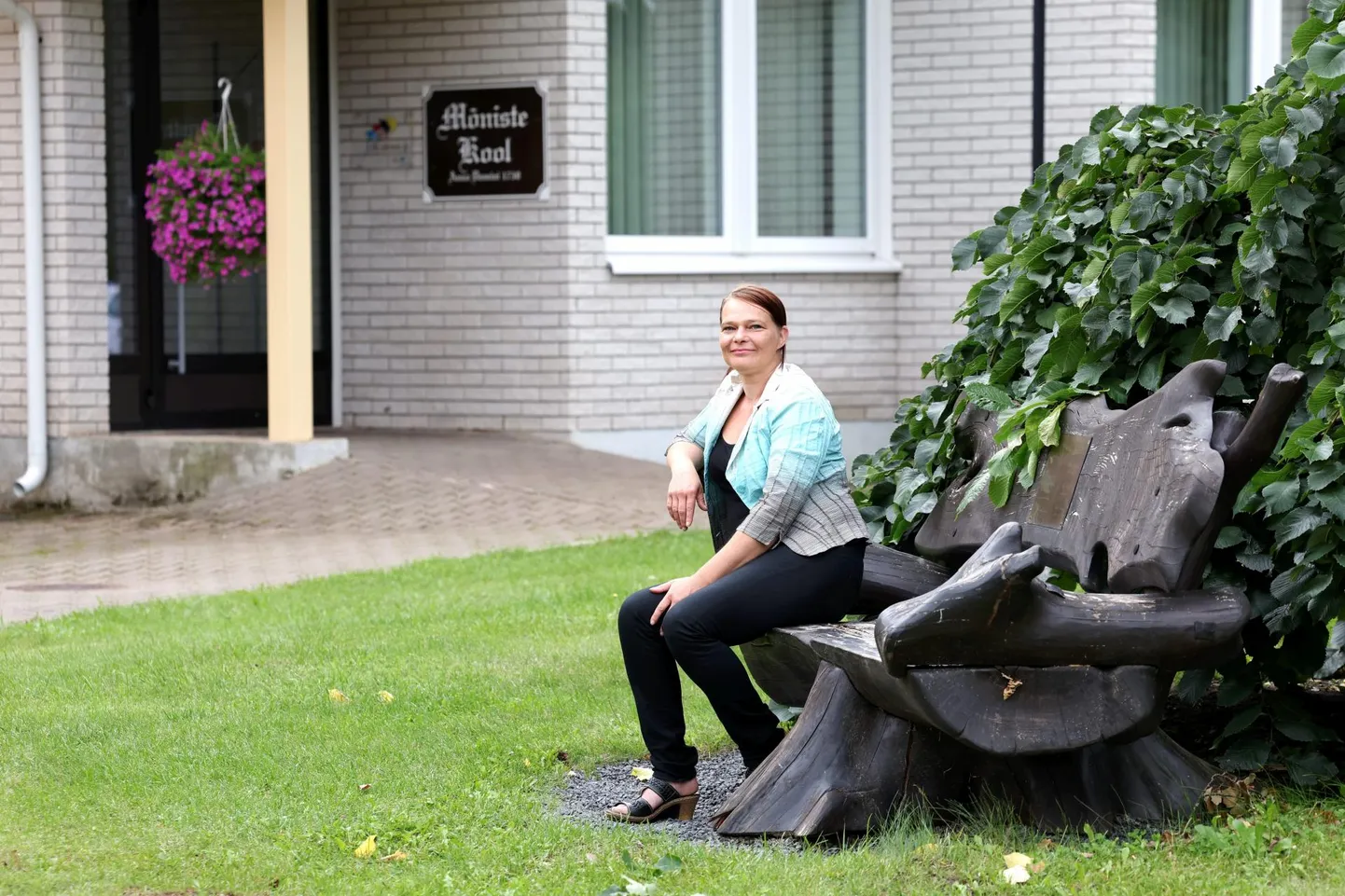 Mõniste kooli direktor Maarika Niidumaa koolihoone ees tarkade mõtete pingil, kus on tahvel kõigi seniste koolijuhtide nimedega.
