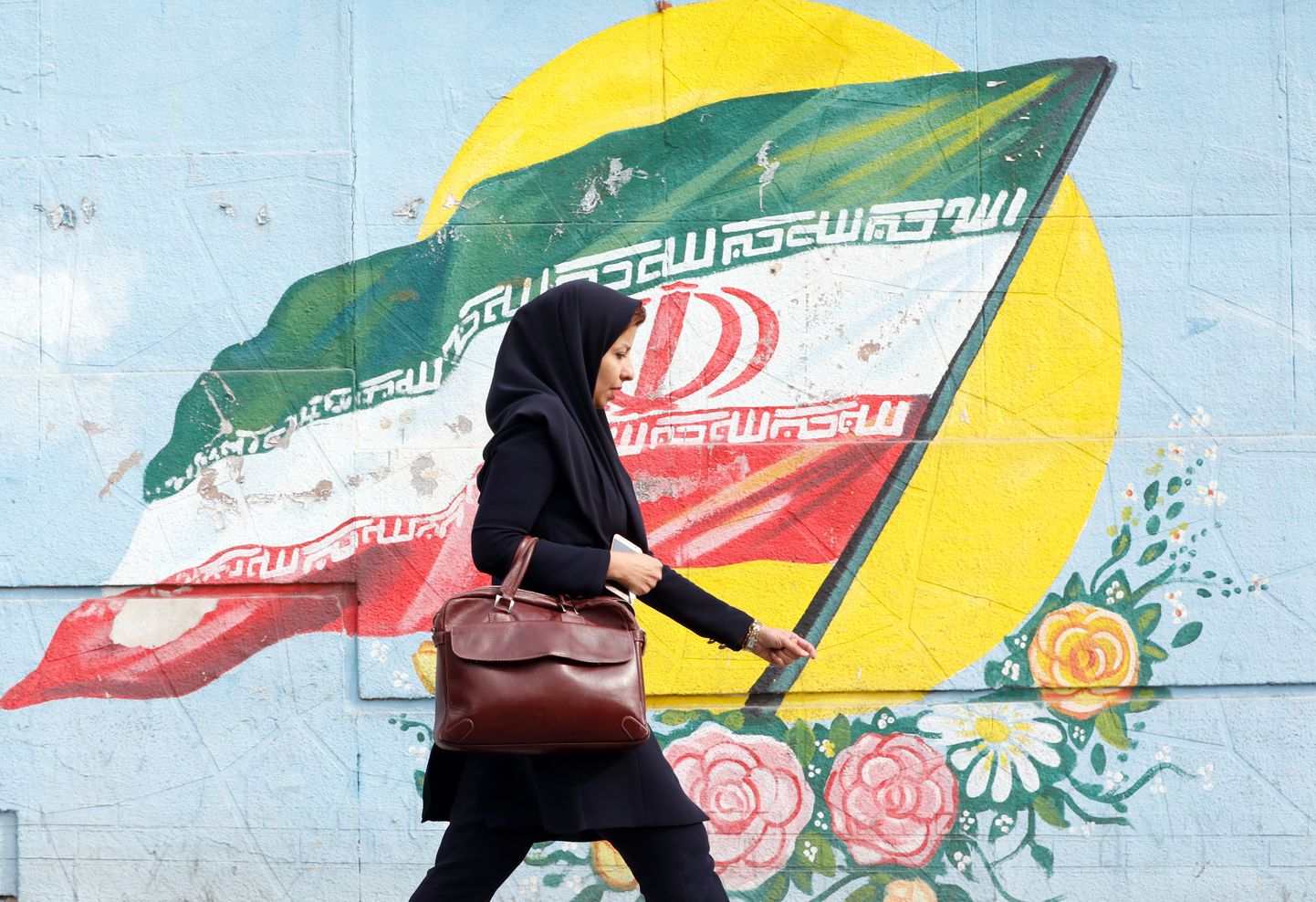 Iraani naine jalutamas Teherani tänaval mööda riigi lippu kujutavast seinamaalingust.