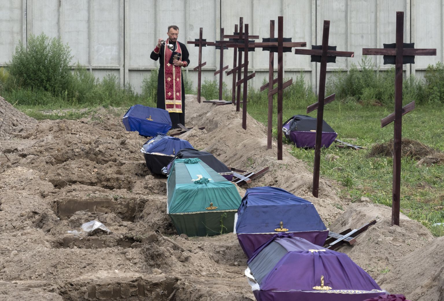 Священник около могил перед погребением 11 неопознанных мирных жителей, которые были эксгумированы после оккупации Бучи российскими войсками. Украина, 11 августа 2022 года.