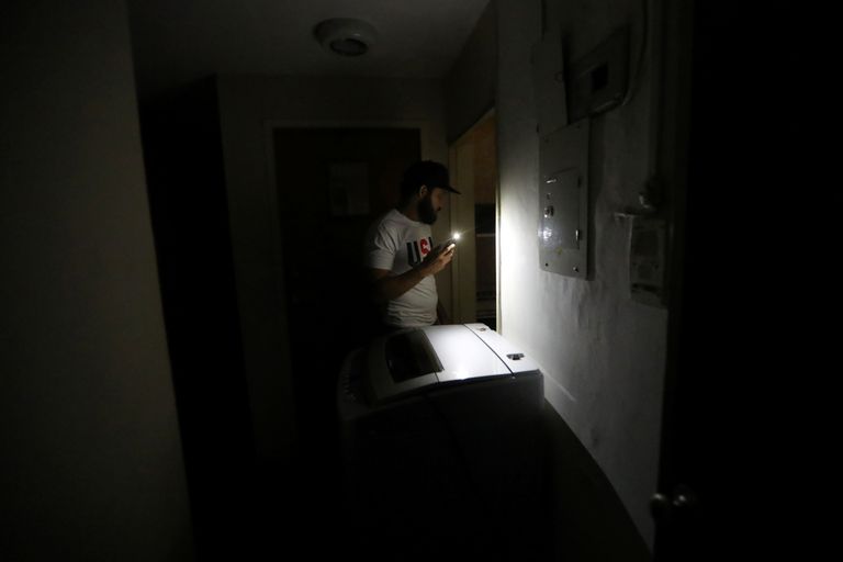 Riigi pealinnas Caracases elav mees näitab pimedas korteris valgust mobiiltelefoni abil.