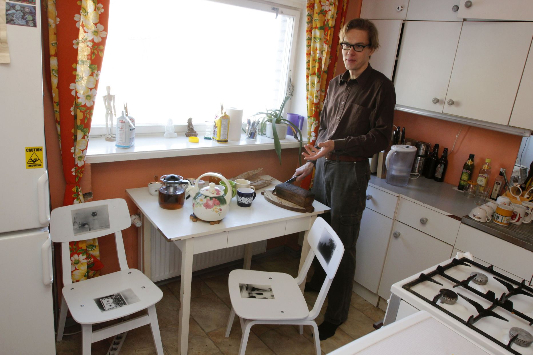 Indrek Grigor lõikab leiba oma köögis, mille laua juures on kaks Martiini fotodega tooli.