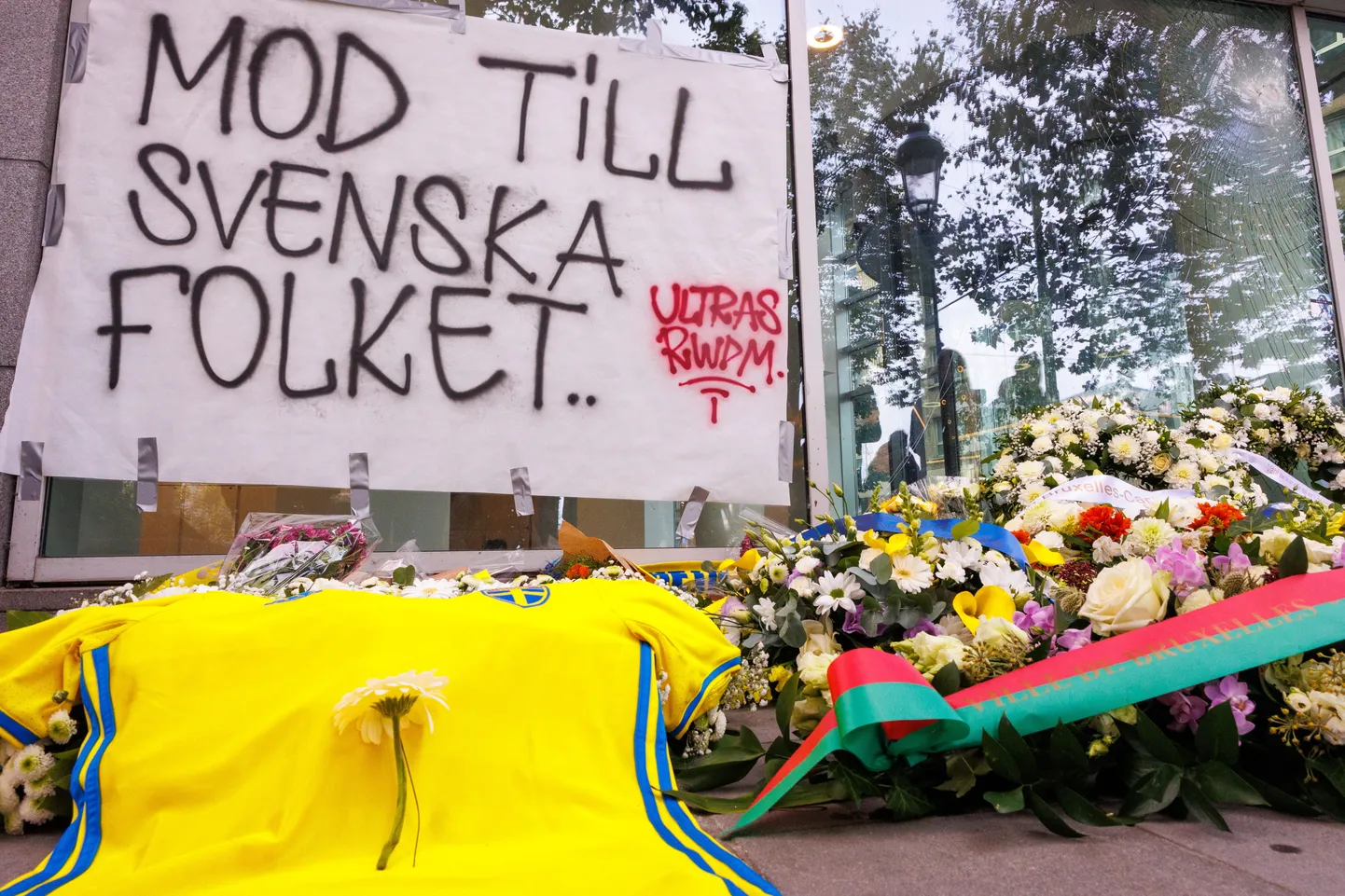 Футболка и цветы сборной Швеции по футболу возложены рядом с плакатом с надписью «Мужество шведского народа» во время поминовения двух шведских футбольных болельщиков, убитых вооруженным преступником в результате теракта в Брюсселе. Мужчина, подозреваемый в убийстве двух граждан Швеции 16 октября, был застрелен полицией во время операции.