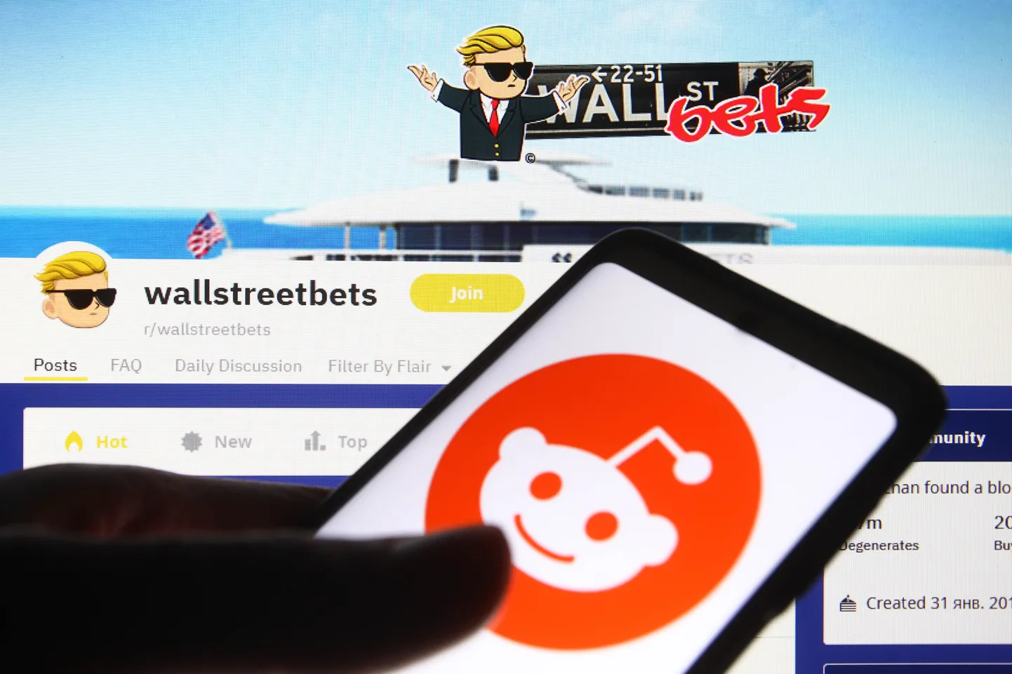 Redditi logo mobiiliekraanil, taustaks arvutiekraan WallStreetBetsi vaatega Redditi suhtluskeskkonnas.