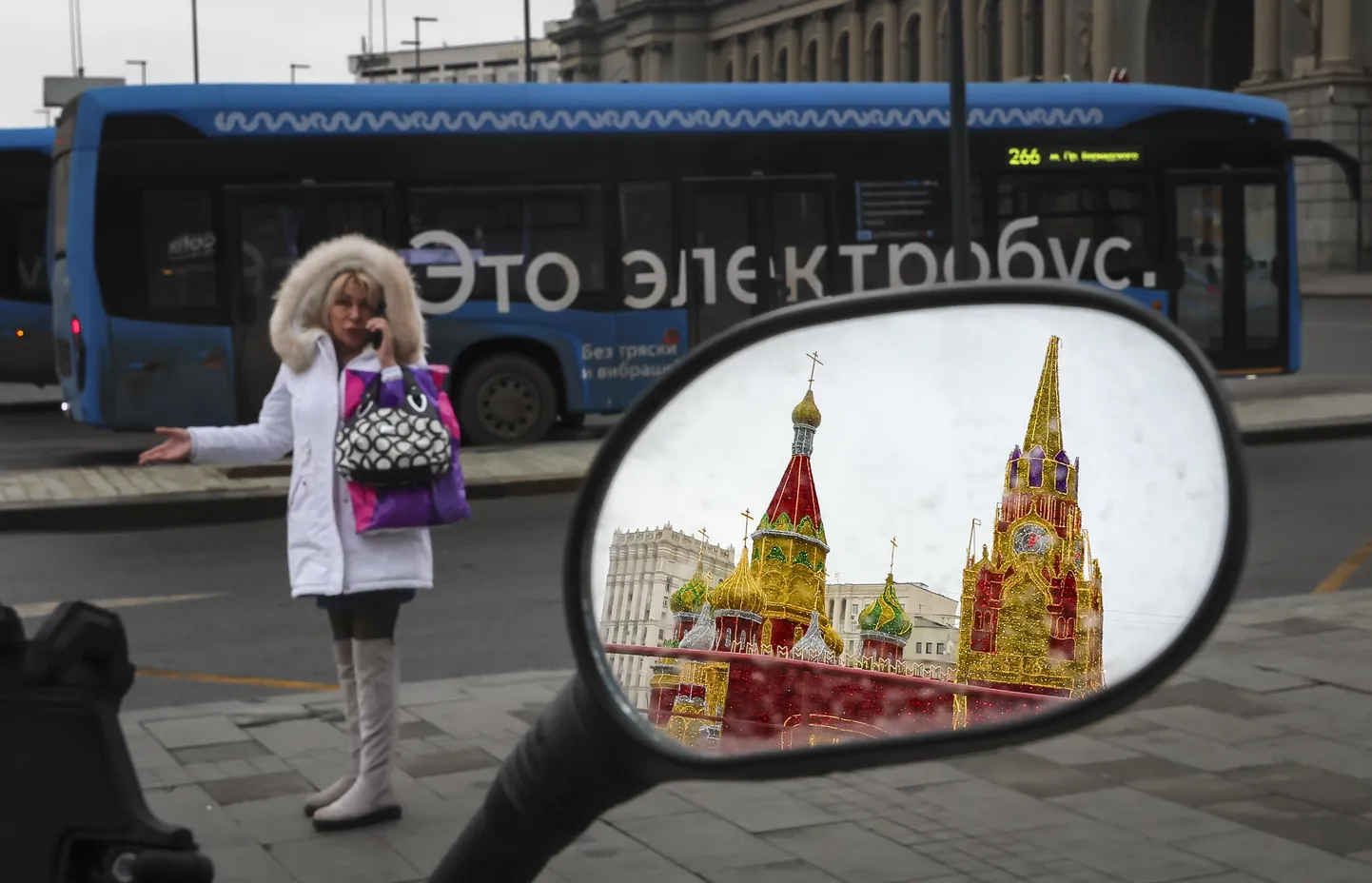 Moskvalanna rääkimas mobiiltelefoniga Kievski raudteejaama juures 30. jaanuaril 2025. Motorolleri peeglist paistab Kremli tornide installatsioon.