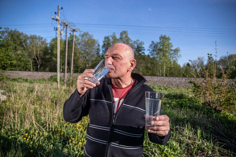 Андрей пьет покупную питьевую воду, в другой руке у него стакан с желтой колодезной водой.