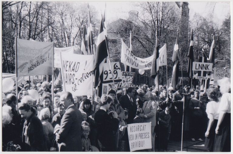 1991. gada pavasaris. Attēlā mītiņš Dubultu laukumā pie Dubultu ev. lut. baznīcas par godu, iespējams, 4. maija deklarācijas par Latvijas Republikas neatkarības atjaunošanu. Kreisajā pusē vīrietis uzvalkā - Jānis Liepiņš.
