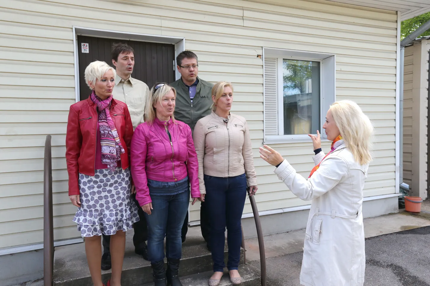 Viis RõõmuSõõmu lauljat kahekümnest – esimeses reas Kerttu Rahe, Anne Laur ja Merle Kõrgesaar ning teises reas Taivo Tali ja Alar Lutsar – laulavad remonti ootava majapidamishoone trepil «Ta lendab mesipuu poole». Dirigeerimist markeerib perekodu juhataja Sirli Peterson.