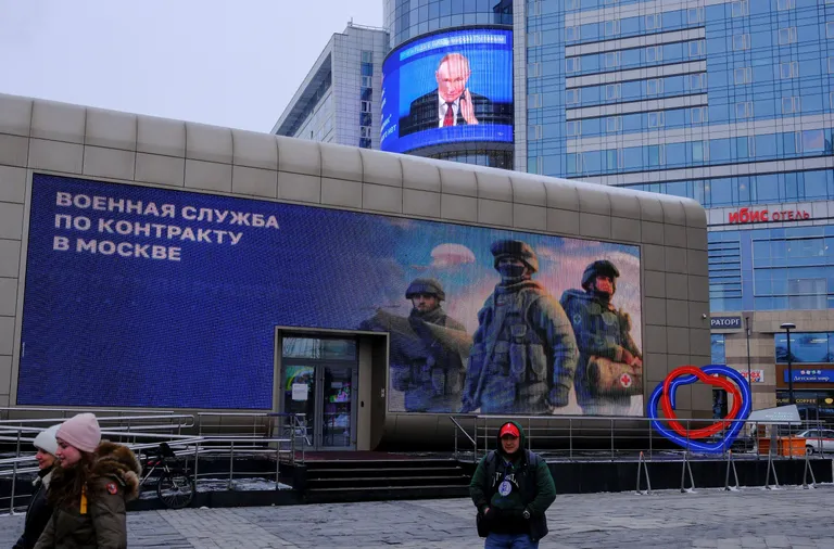 На здании реклама с надписью «Военная служба по контракту в Москве», за ним, на другом здании, экран с лицом Путина.